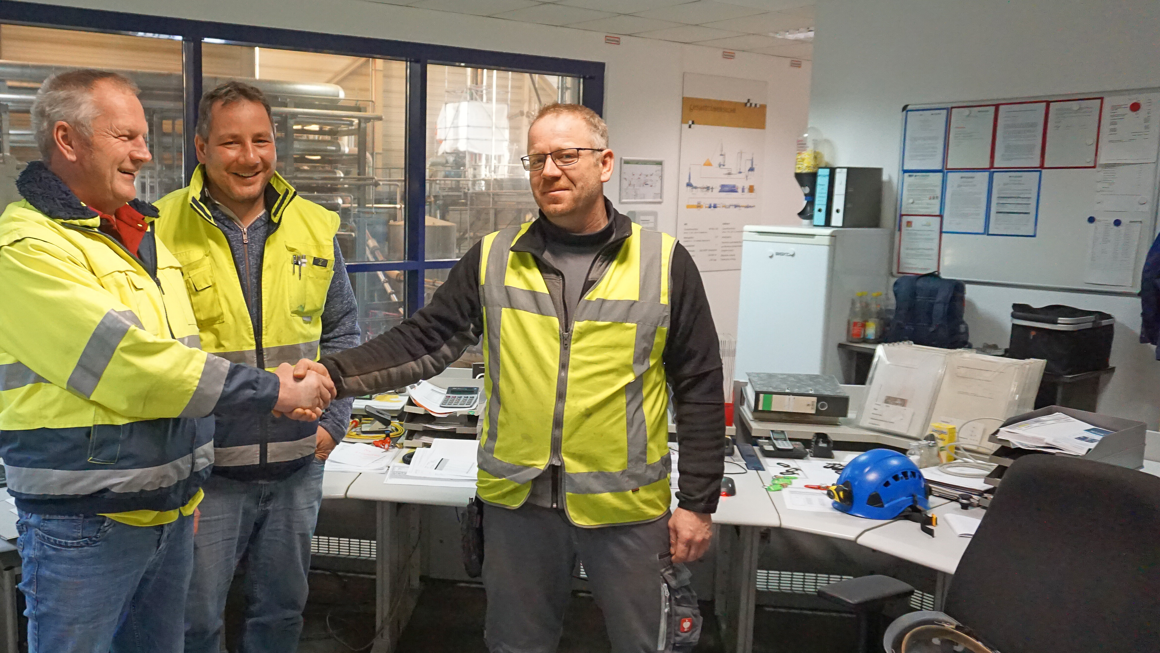 3 people wearing yellow high-visibility vests in the technical room